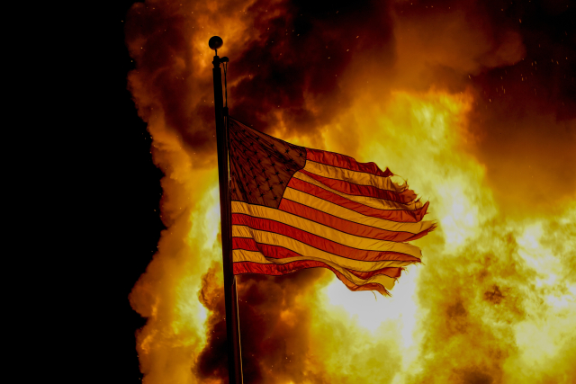 A flag flies over a department of corrections building ablaze during protests, late Monday, Aug. 24, 2020, in Kenosha, Wis., sparked by the shooting of Jacob Blake by a Kenosha Police officer a day earlier. (AP Photo/Morry Gash) ()