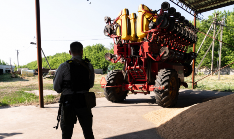 Ozbrojený strážce stojí vedle zemědělského stroje ve skladu kukuřice v Kyjevské oblasti (ČTK/News Pictures/Ukrinform)