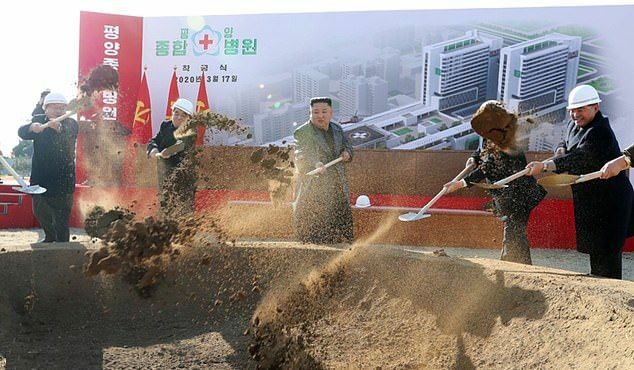 Severokorejský vůdce Kim Čong-un hází hroudu hlíny do vykopané jámy a navozuje představu stavby budovy podle vizuálu, který má za zády.