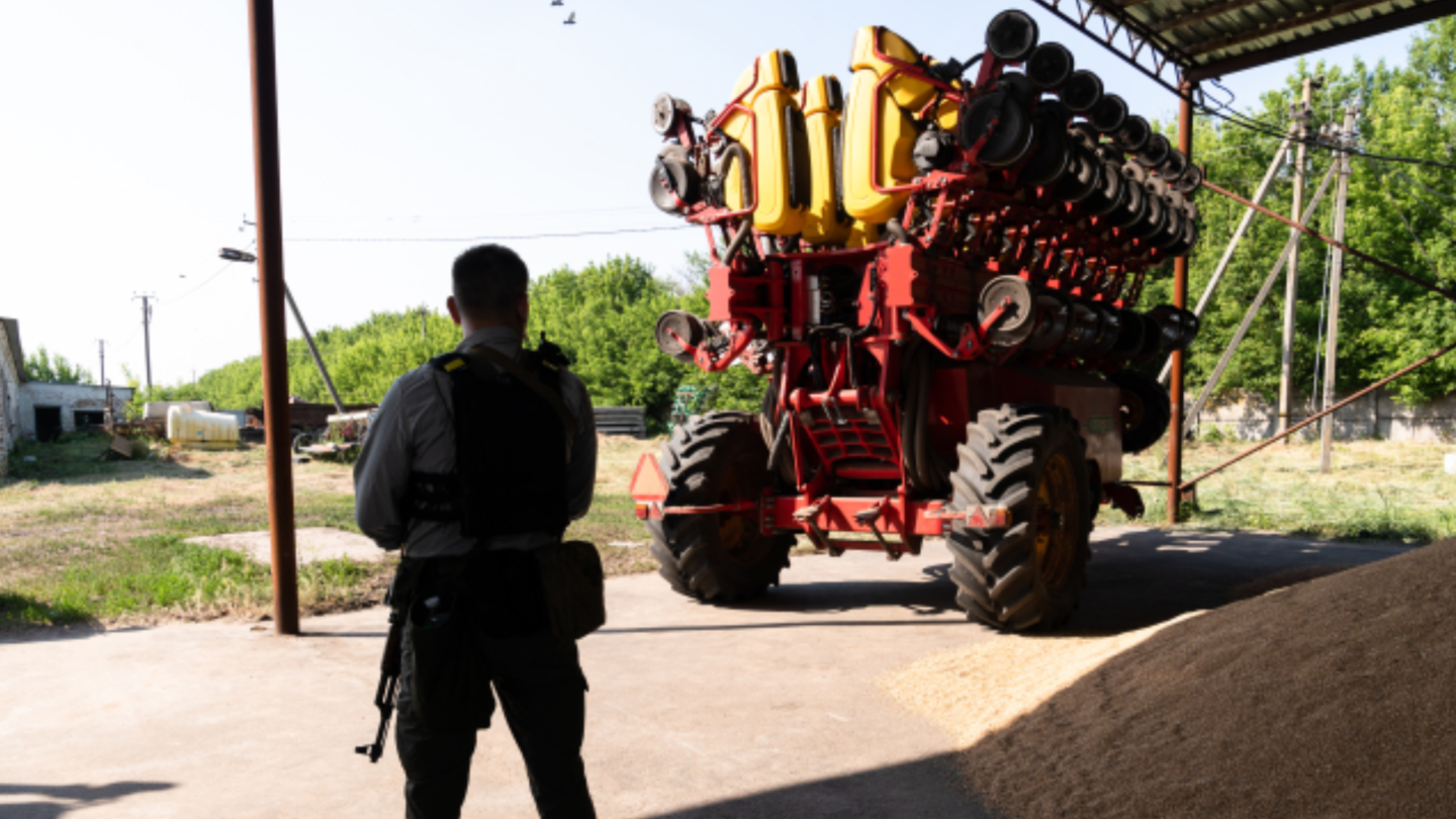 Ozbrojený strážce stojí vedle zemědělského stroje ve skladu kukuřice v Kyjevské oblasti