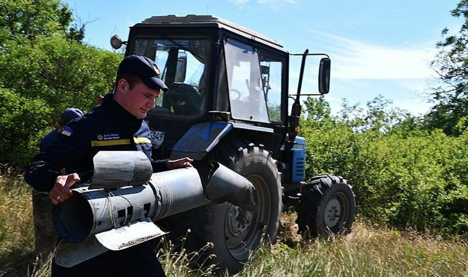 Příslušník Státní pohotovostní služby Ukrajiny odnáší  nevybuchlou ruskou bombu z pole na Ukrajině