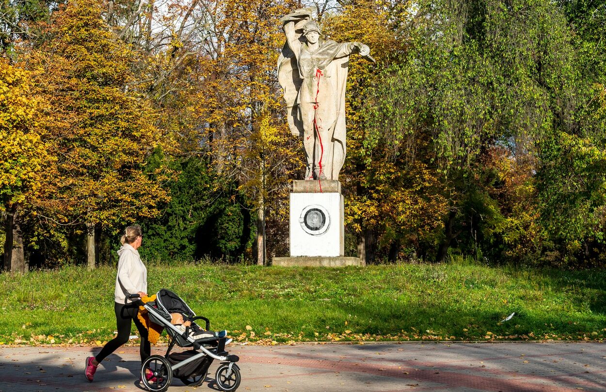 Žena prochází okolo sochy rudoarmějce potřísněné červenou barvou a s namalovanou pračkou na podstavci, 25. října 2022 v Jiráskových sadech v Litoměřicích.