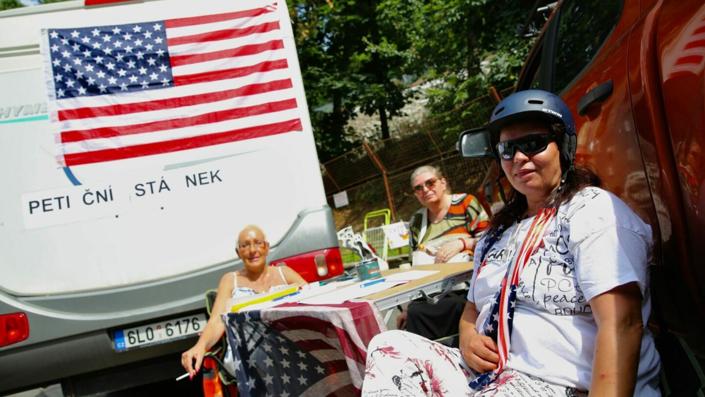 Karavan, osobní auto, stolek, židličky, archy s peticemi, vlajky Spojených států a NATO. Tohle všechno se ve středu 21. června objevilo u chodníku naproti sídlu české vlády. 