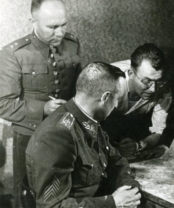 V krytu v Bartolomějské ulici během povstání v květnu 1945. Sedící velitel povstání generál Karel Kutlvašr, Jaromír Nechanský v košili skloněný nad stolem.
